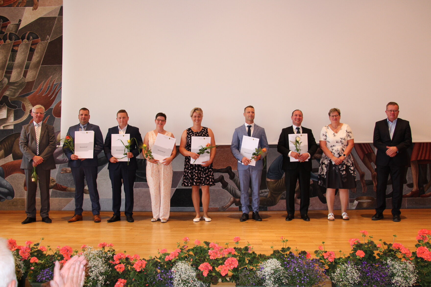 Landwirtschaftsmeisterinnen und Landwirtschaftsmeister stehen auf einer Bühne und halten ihr Zeugnis sowie ihren Meisterbrief in der Hand.
