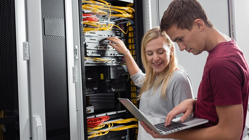 Ein gemischtgeschlechtliches Team von Fachinformatikern arbeitet an Servern in einem Rechenzentrum. Dazu wird ein Laptop verwendet.
