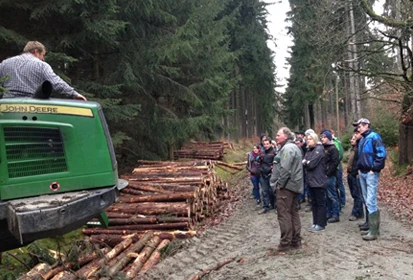 Fachschüler stehen auf einem Waldweg und schauen interessiert der Holzernte zu
