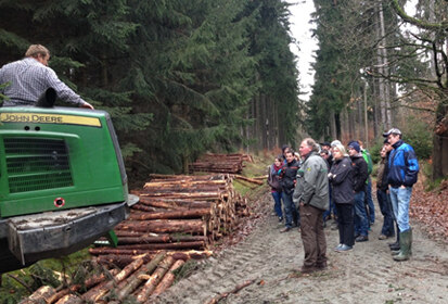 Fachschüler stehen auf einem Waldweg und schauen interessiert der Holzernte zu